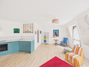 Eine moderne Küche mit türkisfarbenen Schränken, einem roten Teppich, einem blauen Sessel und einem farbenfrohen Sofa.