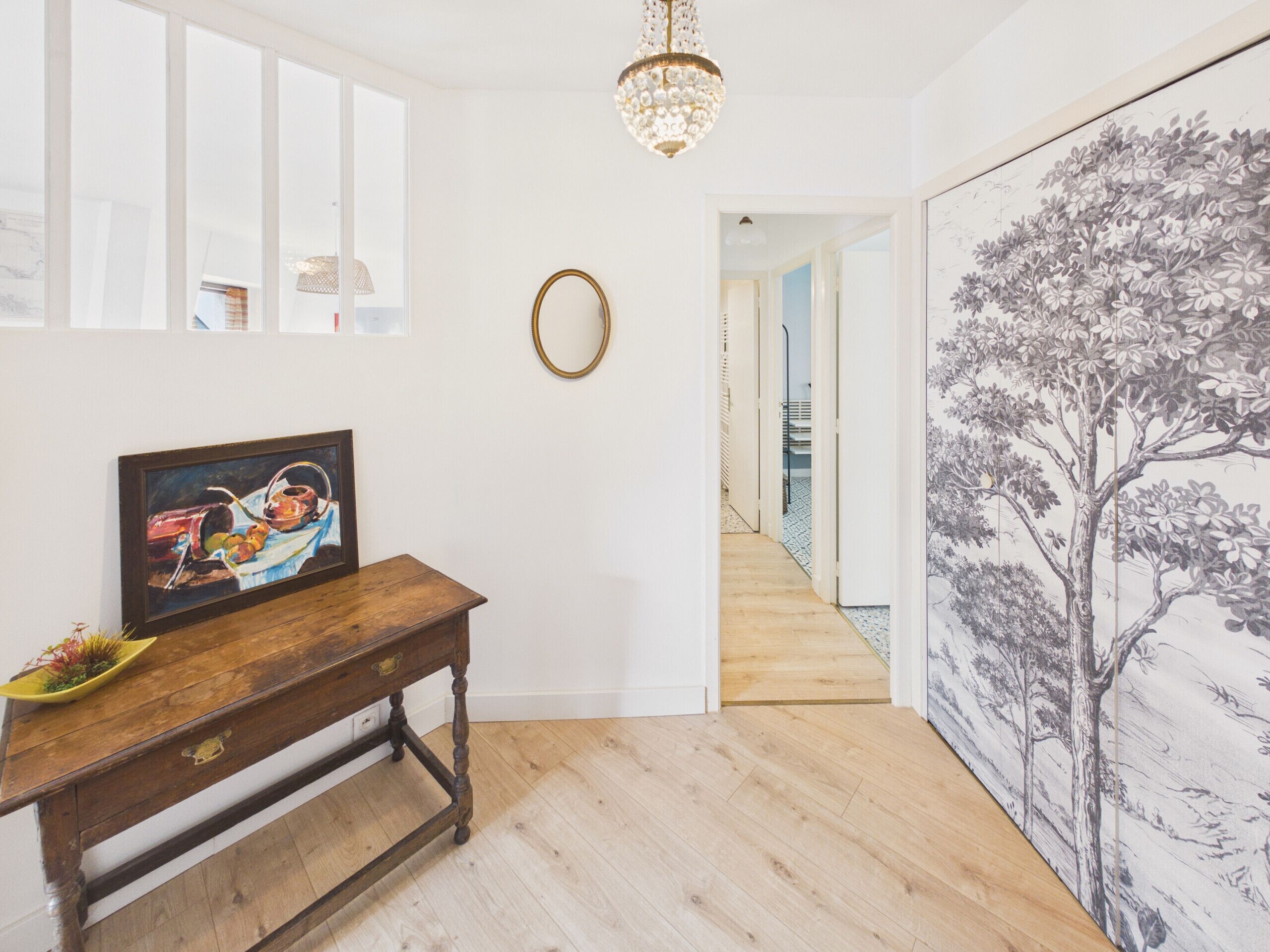 A hallway with a wooden bench, a framed painting, a chandelier, and a large wall mural.