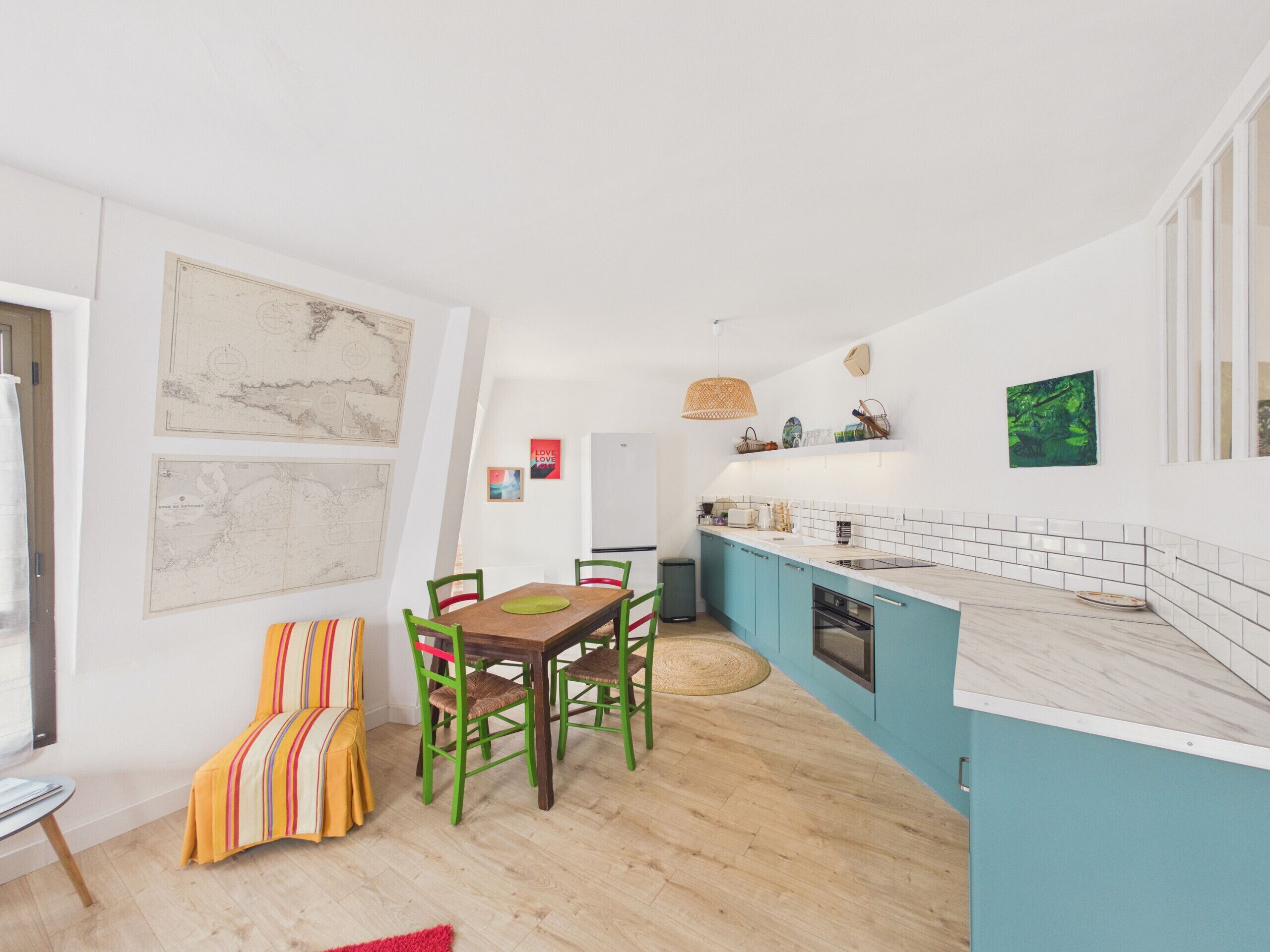 A modern kitchen with teal cabinetry, a wooden dining table, and chairs.