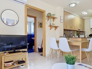 Ein modernes Wohnzimmer mit Fernseher, ein Essbereich mit Stühlen, eine Küche mit Holdekor und ein Flur, der in ein weiteres Zimmer führt.