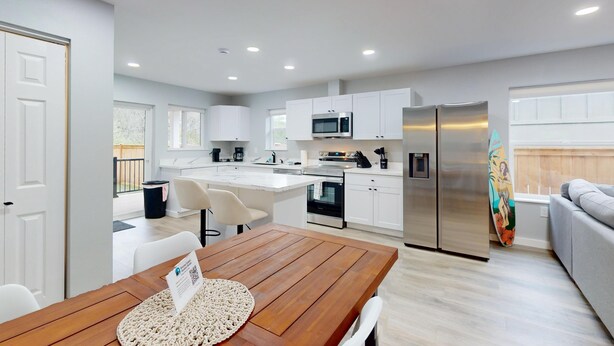 Una cocina moderna con armarios blancos, un refrigerador de acero inoxidable y un comedor con mesa de madera.