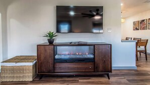 Uma sala de estar moderna com lareira embutida, televisão de tela plana na parede e área de jantar com cadeiras e mesa de madeira.