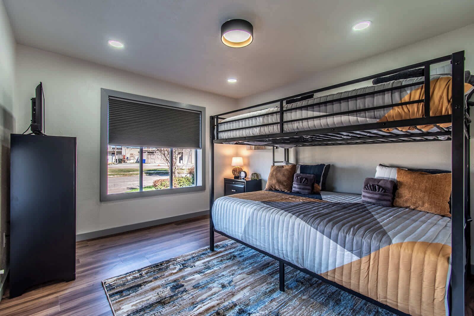 A bunk bed room with a window, a desk, and a lamp.