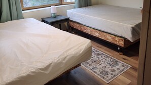 A room with two beds, a window with curtains, a nightstand, and a patterned rug. - 2-bedroom mobile home w/ AC at Elkwood Campground in Wolverine, MI with POOL! (Wolverine)