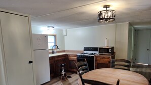 A kitchen with a dining table, chairs, a dog, a refrigerator, a stove, a microwave, and a sink. - 2-bedroom mobile home w/ AC at Elkwood Campground in Wolverine, MI with POOL! (Wolverine)