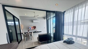 Ett modernt hotellrum med en säng, ett skrivbord med en stol, en tv och ett stort fönster med gardiner.