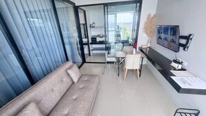 Ett modernt vardagsrum med en soffa, ett matbord, stolar, en tv och en skjutdörr i glas som leder ut till en balkong.