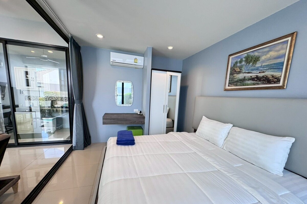 A modern hotel room with a large bed, a bathroom with a mirror, and a painting on the wall.