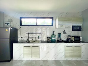A modern kitchen with a built-in sink, a refrigerator, a microwave, and a window above the sink. - Larnthong Villas (Ko Samui)