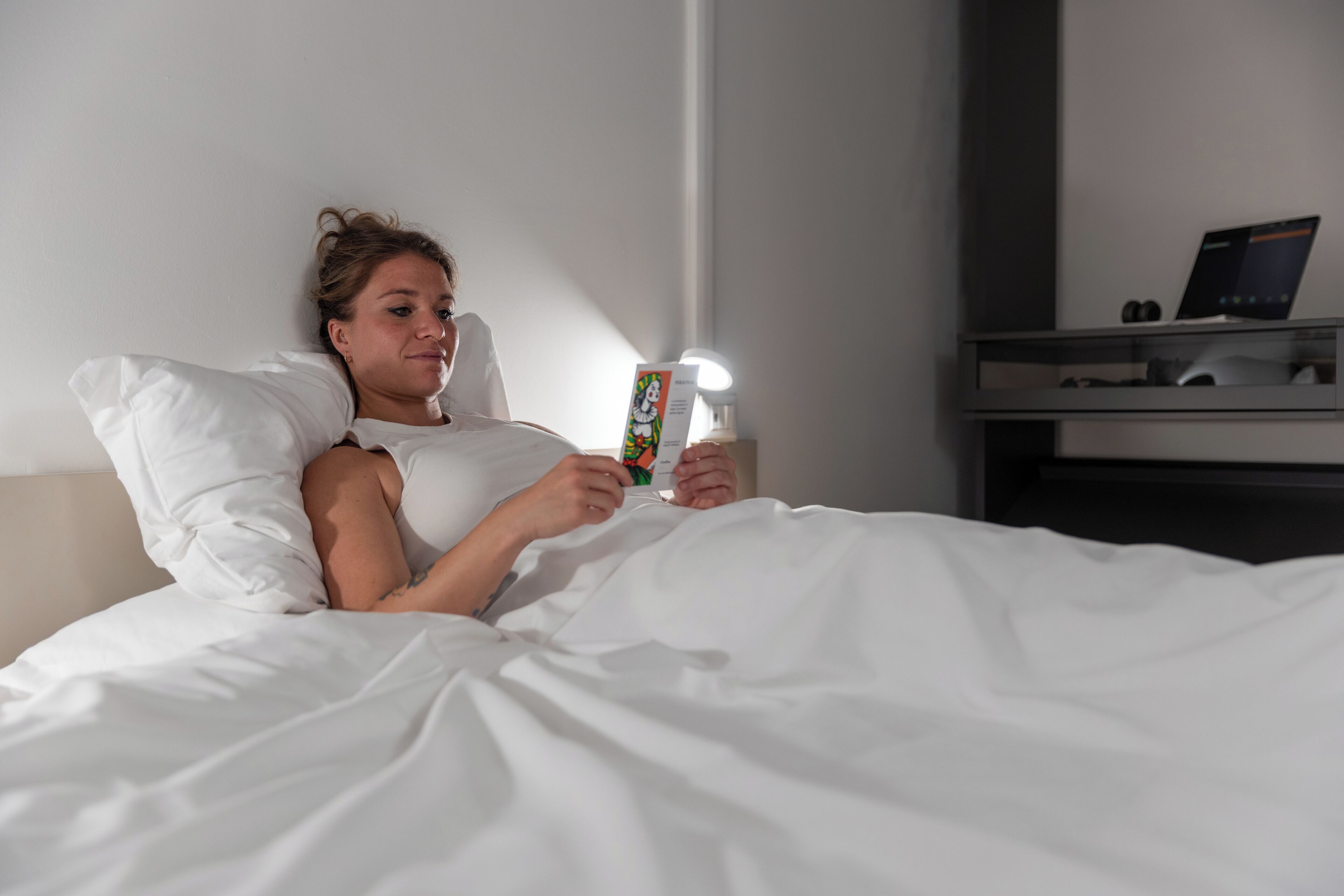A person lying in bed with a laptop on a bedside table.
