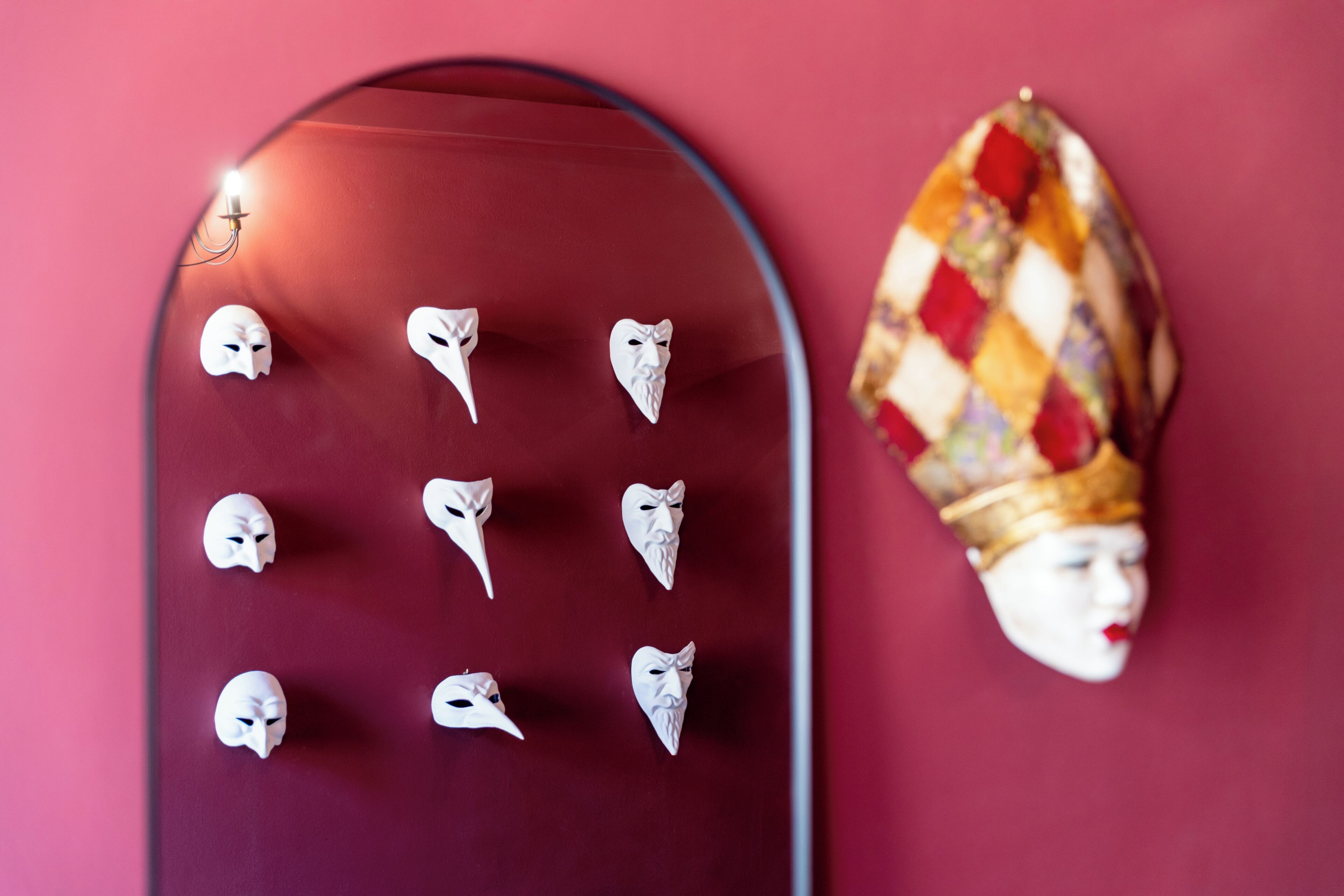 A wall with a series of masks and a single ornate mask.