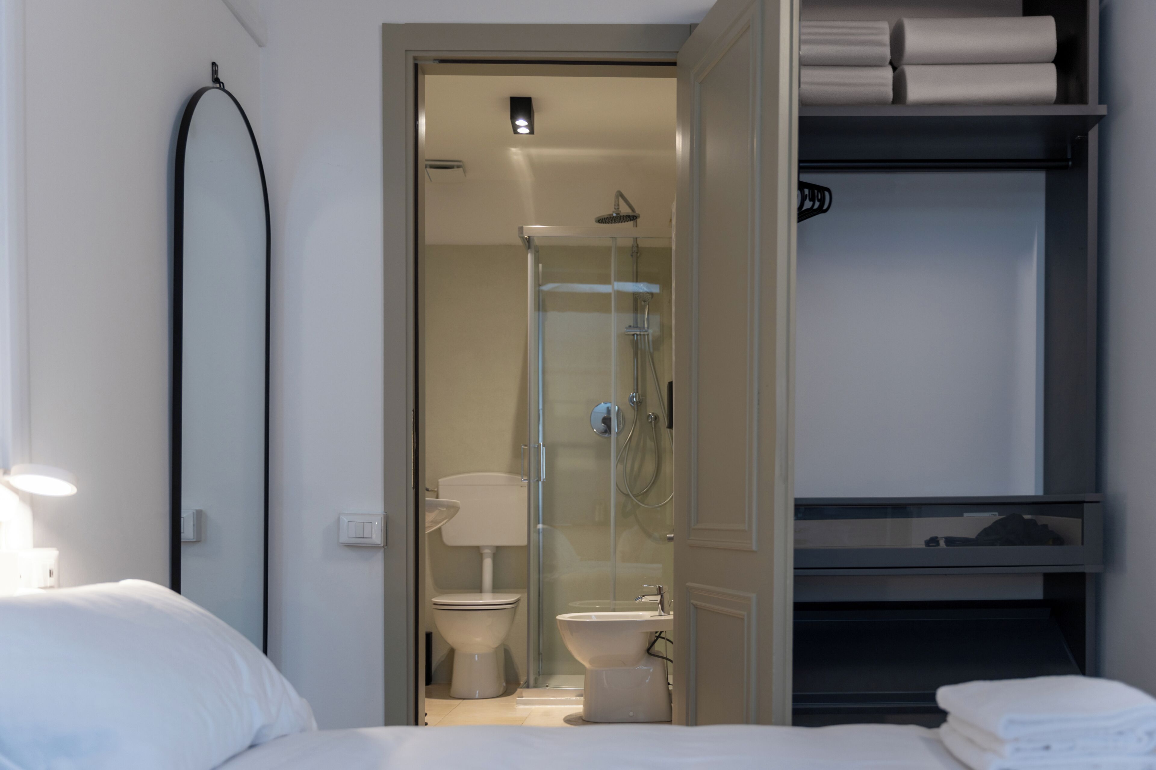 A hotel room with a bed, a bathroom with a toilet, a shower, and a storage shelf.