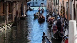A narrow canal with gondolas, buildings with balconies, and a bridge overhead.