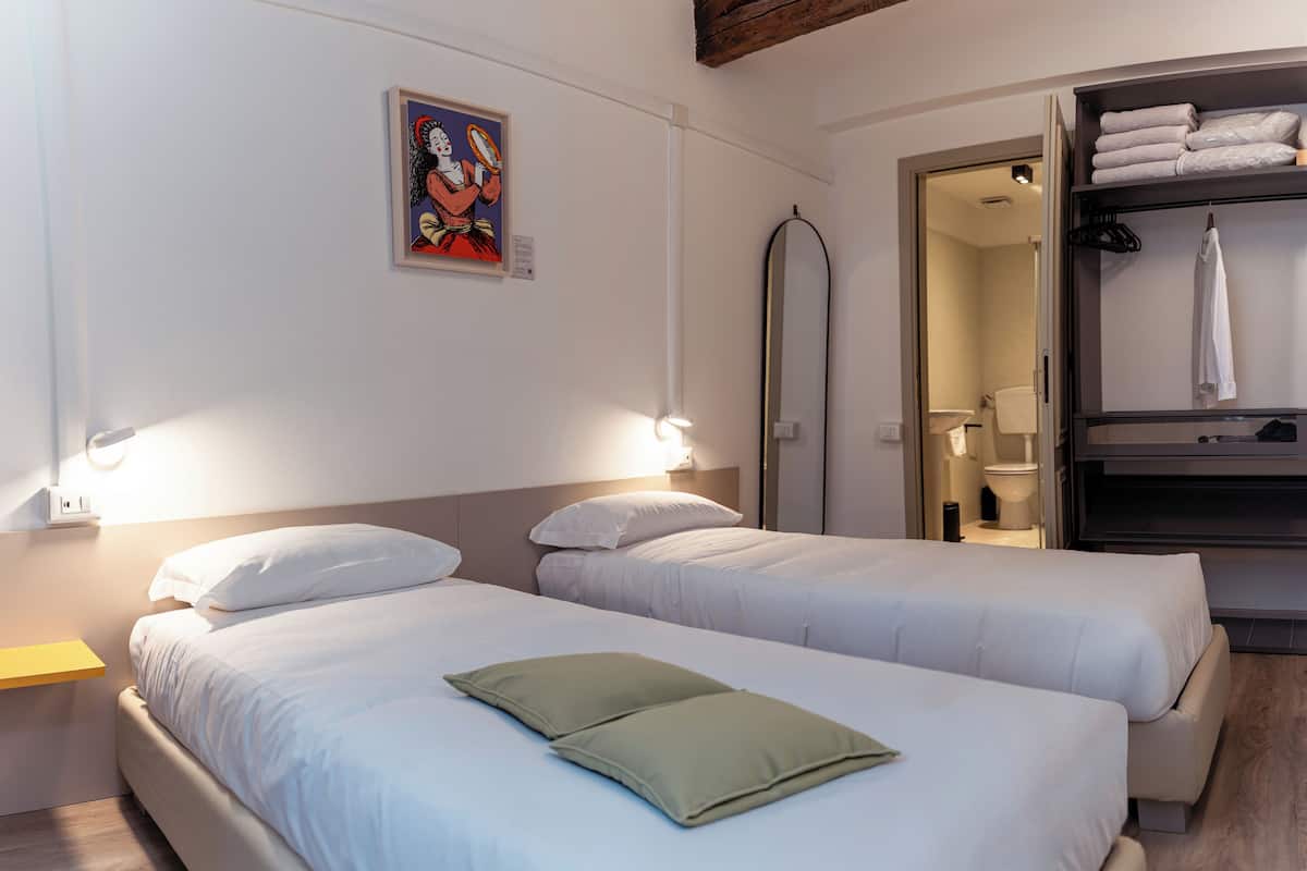 A hotel room with two beds, a painting on the wall, and a bathroom visible through an open door.