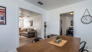 A modern dining area with a wooden table, chairs, and a clock on the wall. - The Coastal Nest Relax & Unwind in Style (Corpus Christi)