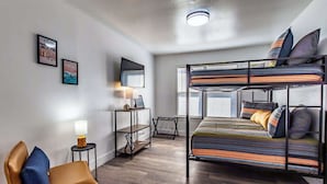 A modern, well-lit room with a bunk bed, a desk, a chair, and a small table with a lamp. - The Coastal Nest Relax & Unwind in Style (Corpus Christi)
