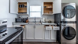 A compact kitchen with white cabinets, a built-in microwave, a stainless steel refrigerator, and a front-loading washer. - The Coastal Nest Relax & Unwind in Style (Corpus Christi)
