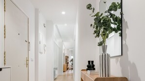 Un couloir avec un plancher en bois, une porte blanche, un miroir et une plante posée sur une console en bois.