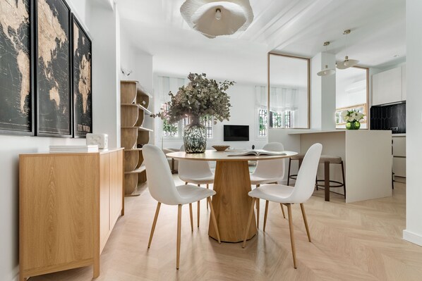 Eine moderne Küche mit einem runden Esstisch, weißen Stühlen und einer zentral platzierten Vase mit Blumen.