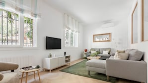 Un salon moderne avec un canapé, une table basse, un téléviseur et une fenêtre équipée de stores.