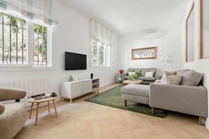 Ein modernes Wohnzimmer mit einer Couch, einem Couchtisch, einem Fernseher und einem Fenster mit Jalousien.