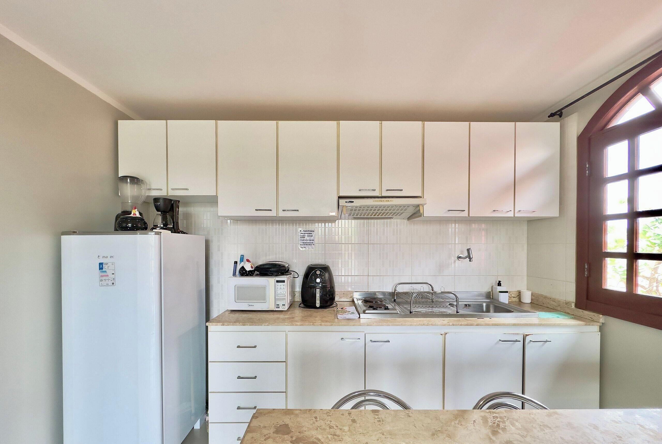 Una cocina compacta con gabinetes blancos, microondas, cafetera y lavabo.