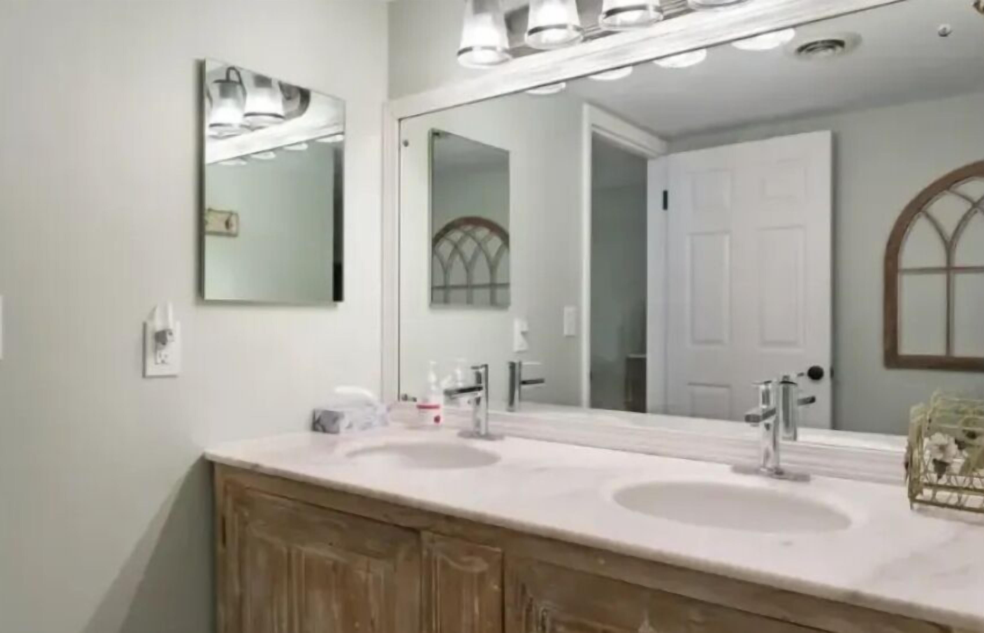 Une salle de bain avec deux lavabos, un grand miroir et un meuble-lavabo en bois.
