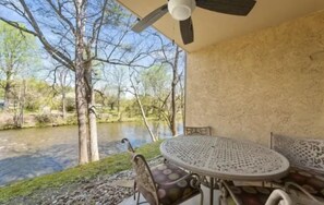 Un espace extérieur aménagé avec une table et des chaises, un ventilateur de plafond et une vue sur une rivière et des arbres.