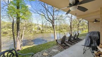 A covered outdoor area with a view of a river, chairs, a grill, and a ceiling fan.