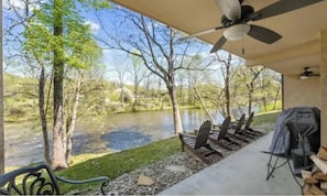 A covered outdoor area with a view of a river, chairs, a grill, and a ceiling fan.
