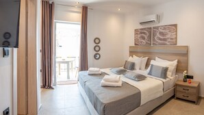 A bedroom with a bed, bedside tables, an air conditioning unit, and a view to the outside.