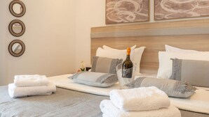 A neatly made bed with white and gray linens, a bottle of champagne, and decorative mirrors on the wall.