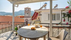 A balcony with a round table, chairs, a clock tower, and a satellite dish in the background.