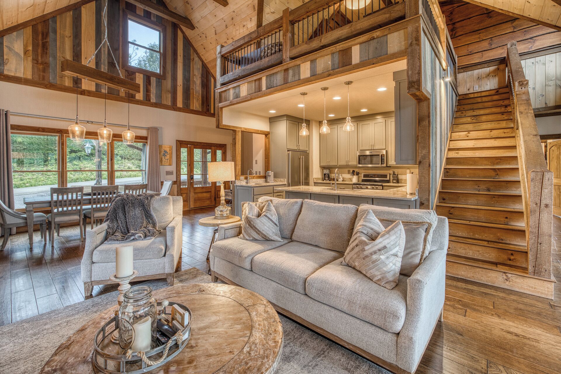 A spacious living area with a large sofa, a coffee table, and a dining table with chairs. A kitchen is visible in the background with modern appliances.