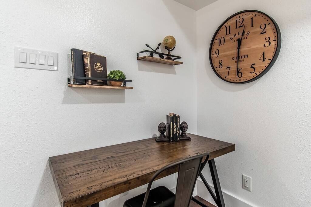 A wooden desk with a globe and books on a shelf, a large wall clock, and a power outlet.