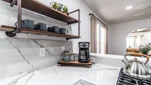 A kitchen with marble countertops, a coffee maker, jars, and a kettle on a stove. - Tranquil Terrace - Duplex #1 (Corpus Christi)