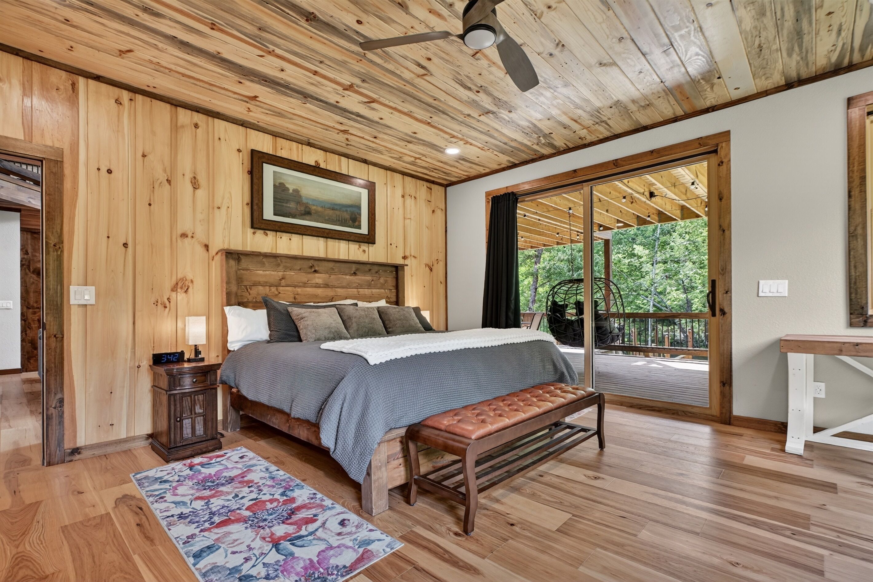 Dormitorio con paneles de madera, una cama, un banco, una mesita de noche y vistas al exterior.