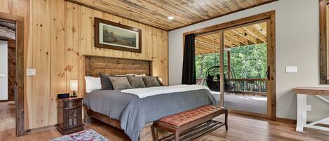 Dormitorio con paneles de madera, una cama, un banco, una mesita de noche y vistas al exterior.