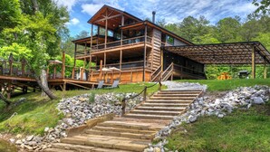Una baita in legno con veranda, sedute all'aperto e una scala in pietra che conduce a un'ulteriore terrazza in legno.