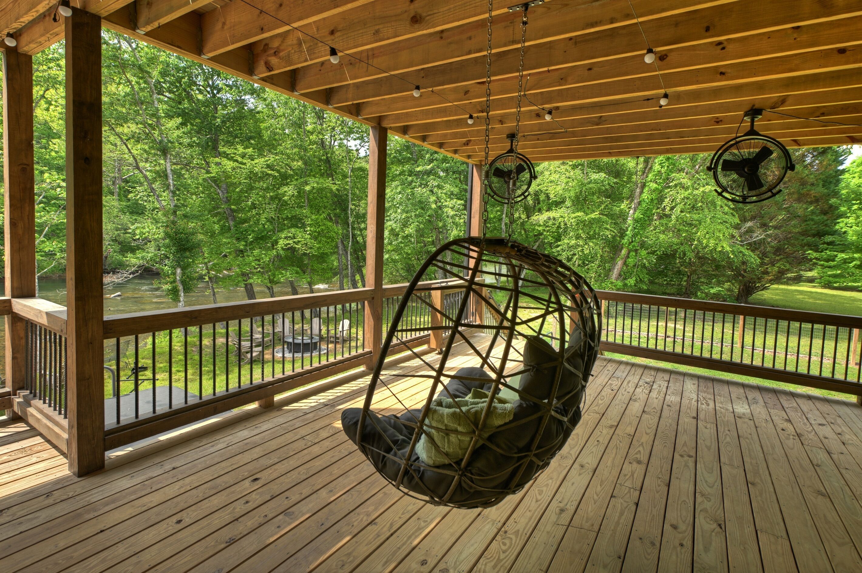 A wooden deck with a hanging chair, a railing, and a view of a forested area.