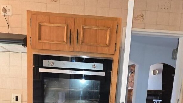 Eine Küche mit Holzschränken, einem Doppelbackofen und einem gefliesten Boden.