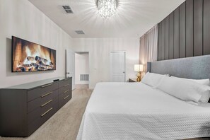 Experience a beautifully designed bedroom with a cozy king-size bed against a striking dark wall. An elegant chandelier adds warmth, enhancing the soft bedding and modern entertainment setup for your ultimate relaxation. - 6BR house sleeps 16 with private pool (Davenport)