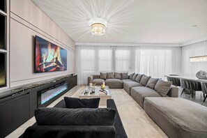 This spacious living room invites relaxation with its plush gray sectional. The soft glow from the stylish chandelier and modern electric fireplace creates a cozy ambiance, perfect for unwinding after your day of adventure. - 6BR house with private pool in Solterra Resort (Davenport)