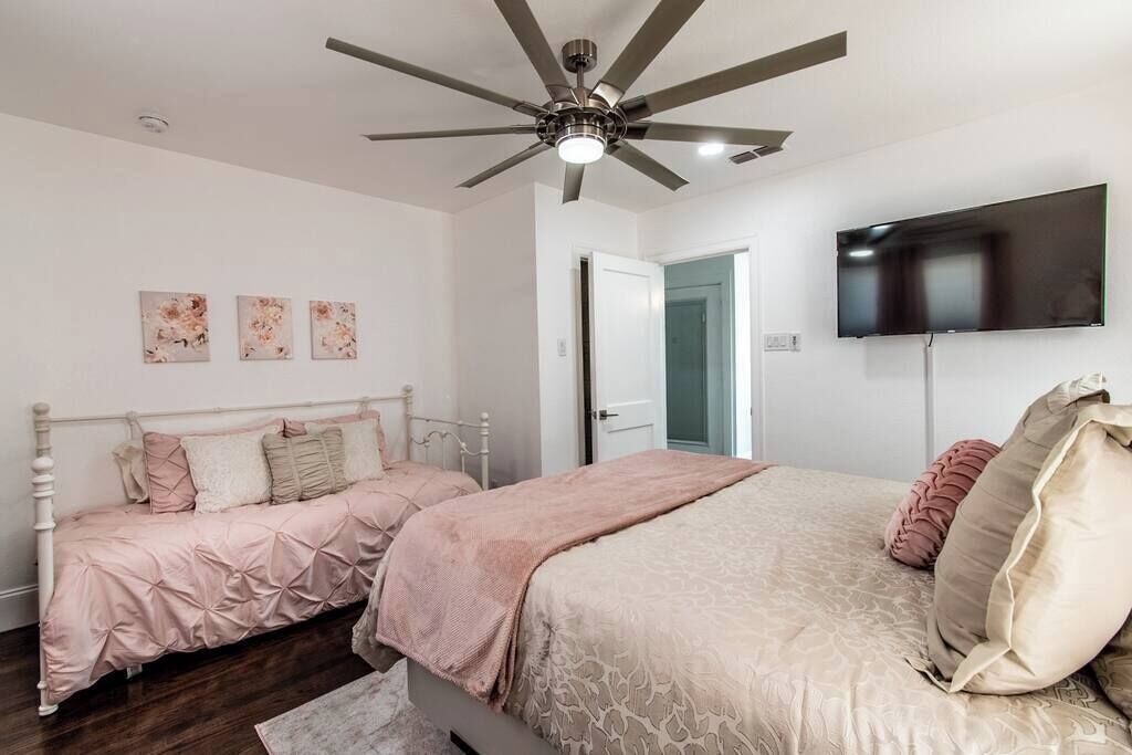 A bedroom with two beds, a ceiling fan, a TV, and a door leading to another room.