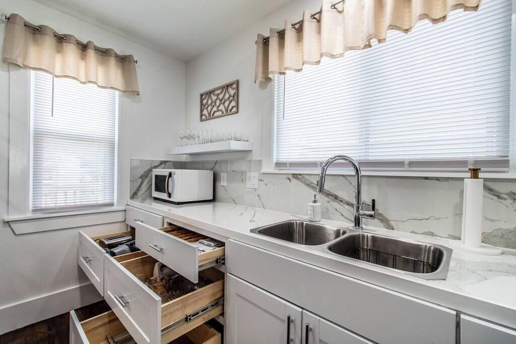 A modern kitchen with white cabinetry, a stainless steel sink, a microwave, and a built-in wine rack.