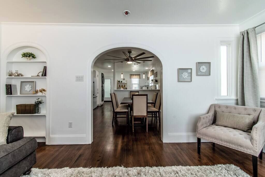 A spacious living room with a dark hardwood floor, a grey sofa, a beige armchair, and a white shag rug.