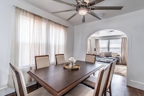 Uma área de refeições com uma mesa de madeira escura, cadeiras bege e um ventilador de teto.