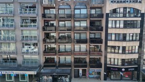 A multi-story building with balconies, a ground-level shop, and a visible restaurant sign. - Sunny Coastal Apartment for 6 (Koksijde)