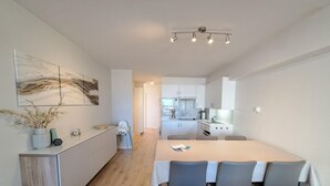 A modern kitchen with a dining area, white cabinetry, and a central island. - Sunny Coastal Apartment for 6 (Koksijde)