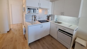 A compact kitchen with white cabinets, a microwave, a coffee maker, a sink, and a stove. - Sunny Coastal Apartment for 6 (Koksijde)